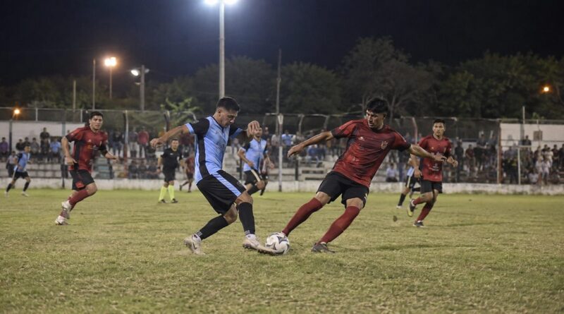 Jugadores disputan una pelota durante un partido nocturno en una cancha regional.